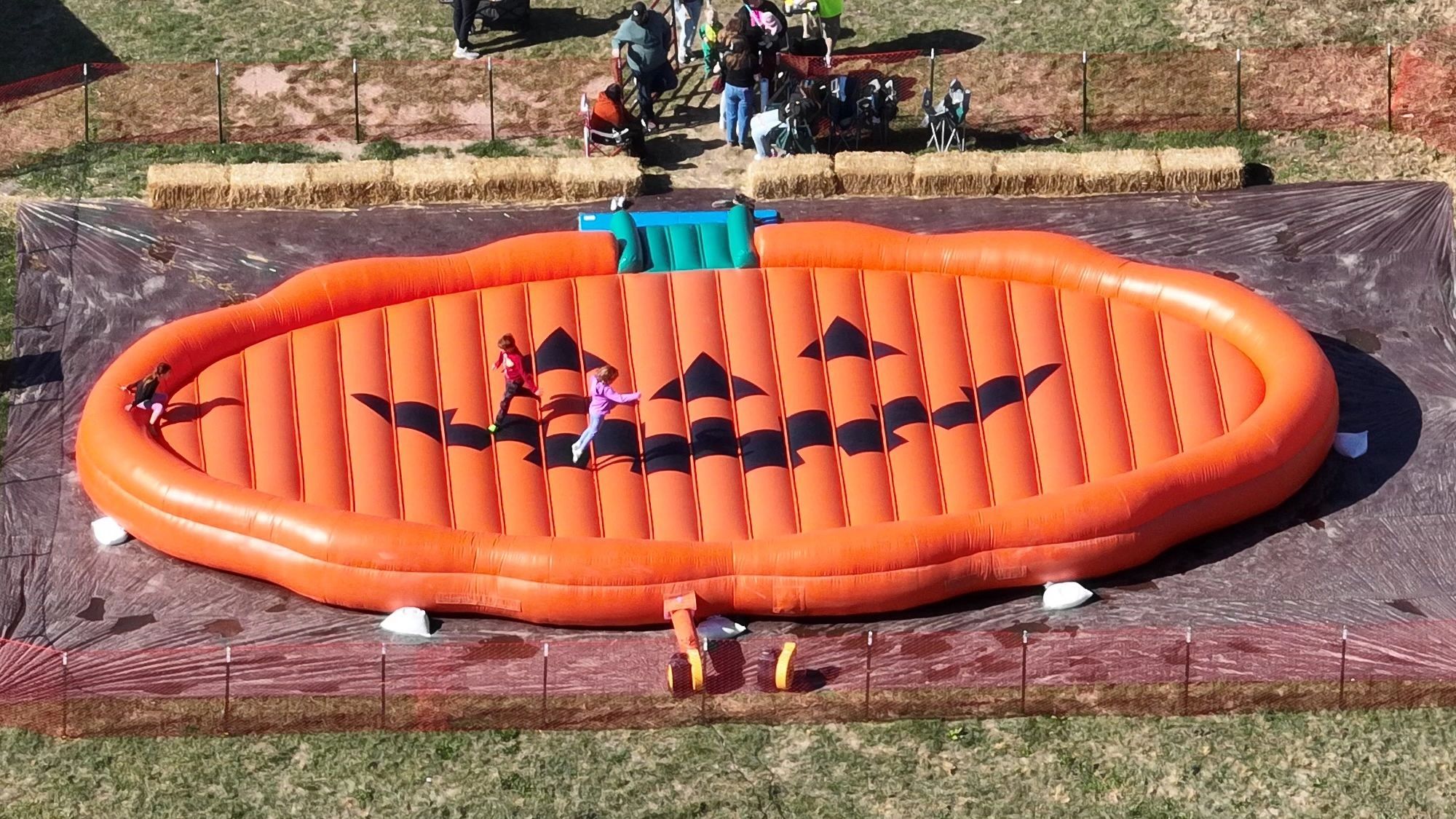 Looking straight down on the giant jack-o'-lantern bounce pillow, with kids jumping on its glowing face